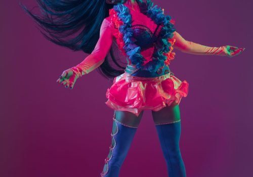 Summertime. Hawaiian brunette model on purple studio background in neon light. Beautiful women in traditional clothes smiling, dancing and having fun. Bright holiday's, celebration colors, festival.