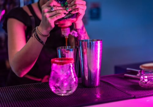 Bartender mixing ingredients in a cocktail mixer in the counter of a bar with neon lights