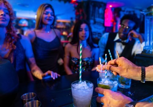 Bartender adding finishing touches to refreshing cocktails at a busy nightclub, watched by patrons